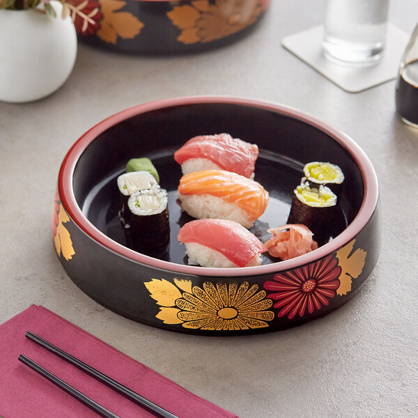 A black sushi tray with a red floral design holding sushi on a table.