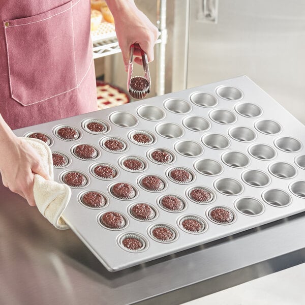 A person putting chocolate cupcakes in a Baker's Mark mini muffin and cupcake pan.