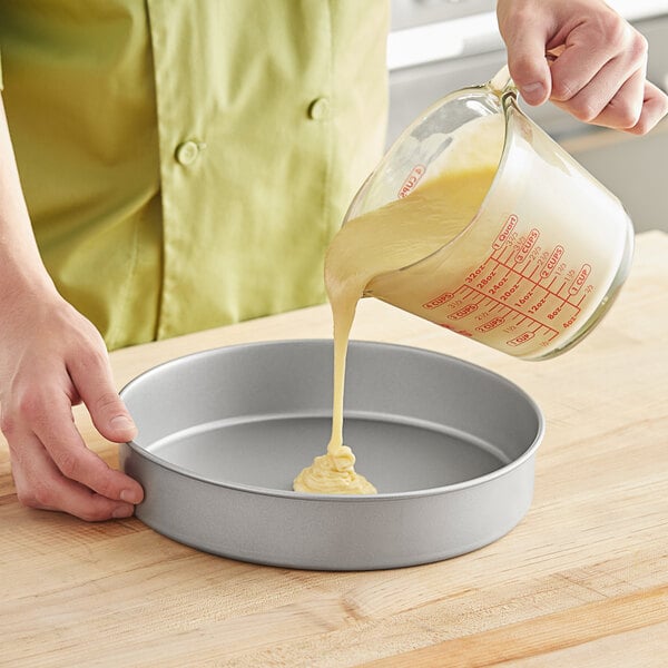 A person pouring batter into a Baker's Mark round cake pan.