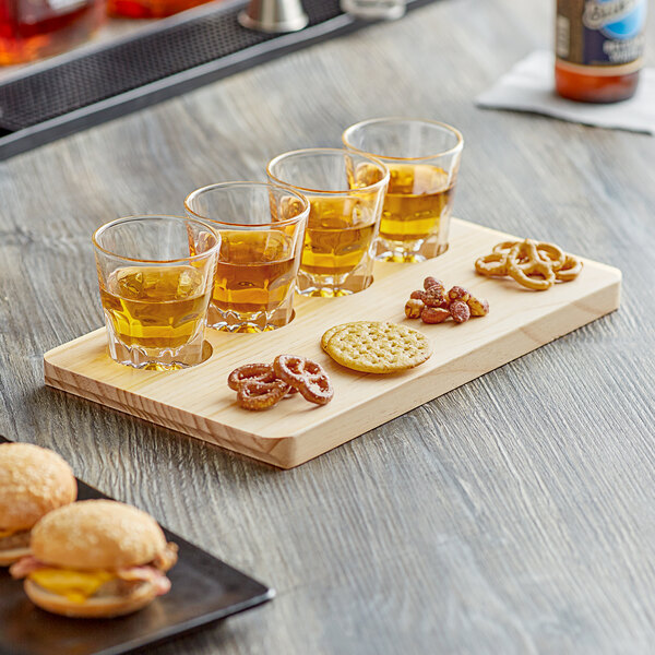 An Acopa natural wood flight tray with four Acopa espresso glasses filled with liquid on a wooden table.