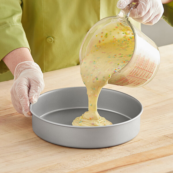 A person pouring Baker's Mark cake batter into a round cake pan.