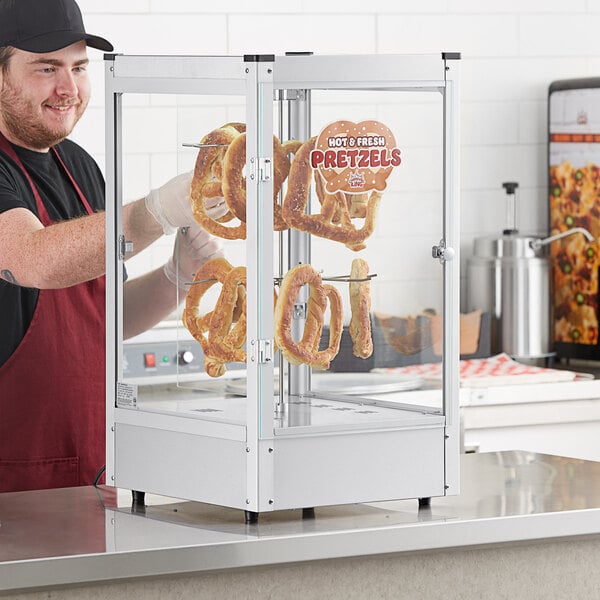 A man holding pretzels in a Carnival King countertop display case.