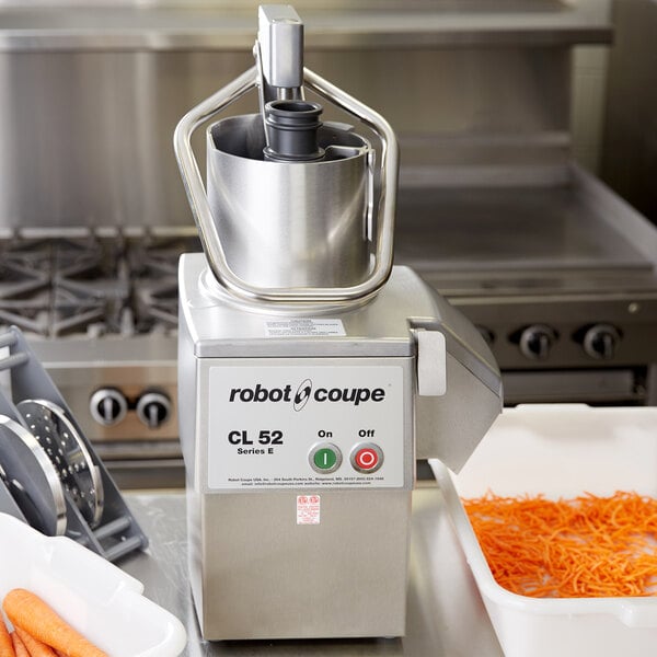A Robot Coupe food processor with a full moon pusher processing carrots.