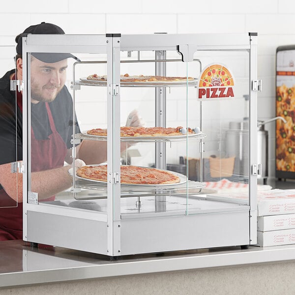 A man in a black hat and apron putting pizzas in a Carnival King countertop pizza display case.