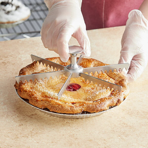 A hand using a Choice 9" Aluminum Pie and Cake Marker to cut a pie.