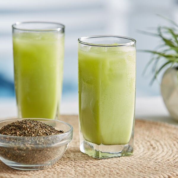 A glass of ChaTraMue Thai green milk tea next to a bowl of green seeds.