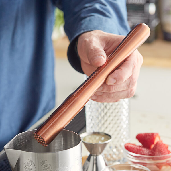 A person using an Acopa copper stainless steel muddler with strawberries in a metal container.