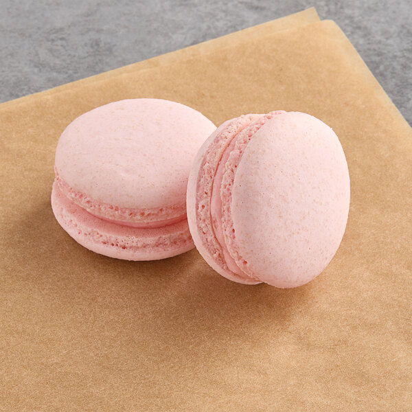 Two pink Macaron Centrale vegan rosewater raspberry macarons on a brown surface.