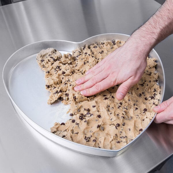 A hand pressing cookie dough into an American Metalcraft heart shaped cake pan.