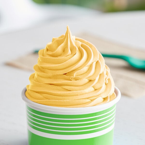 A close up of a cup of yellow frozen yogurt with a green and white background.