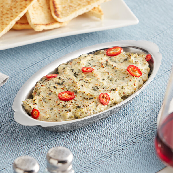 A Choice stainless steel oval au gratin dish with food and a glass of wine.