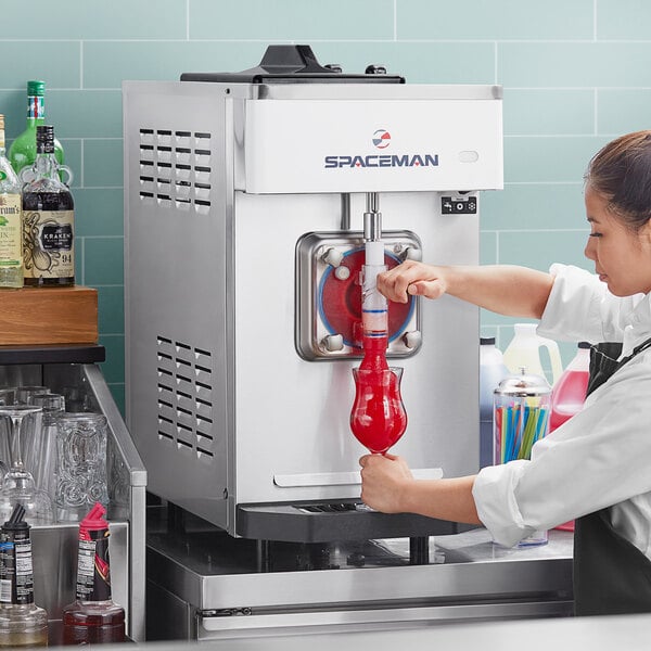 A woman using a Spaceman slushy machine to pour a red drink.