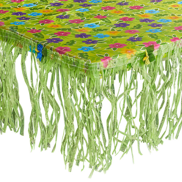 A green tablecloth with fringes and flowers on it.
