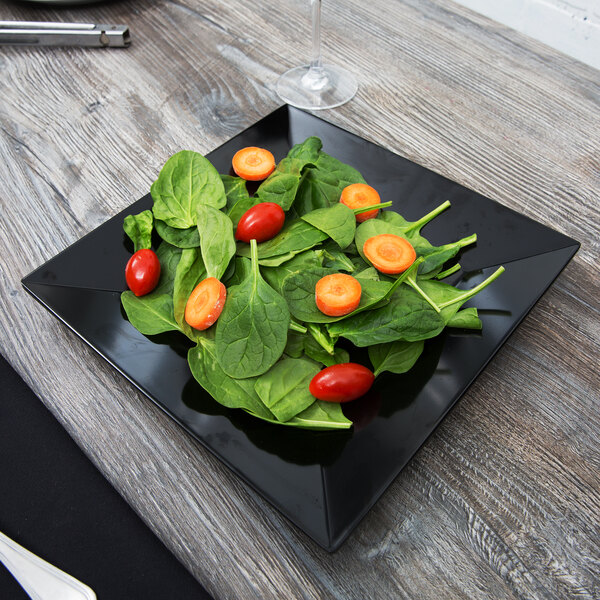 A black GET Siciliano square plate with spinach and tomatoes on a table.