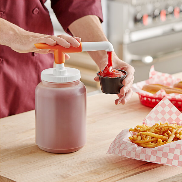 A person using a Choice Condiment Pump to pour red liquid into a container of fries.