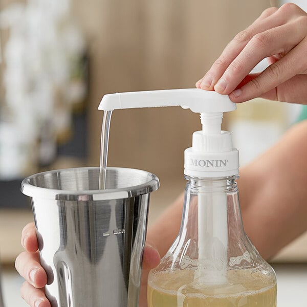 A hand using a Monin syrup pump to pour liquid into a metal cup.
