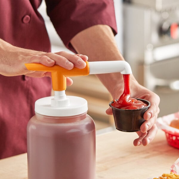A person using a Choice Maxi Pelican condiment pump to pour sauce into a container.