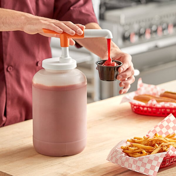 A person using a Choice condiment pump to pour ketchup into a plastic container of fries.
