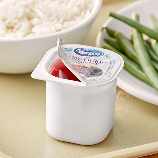 A white container with an open lid filled with red liquid and yogurt with rice in the background.