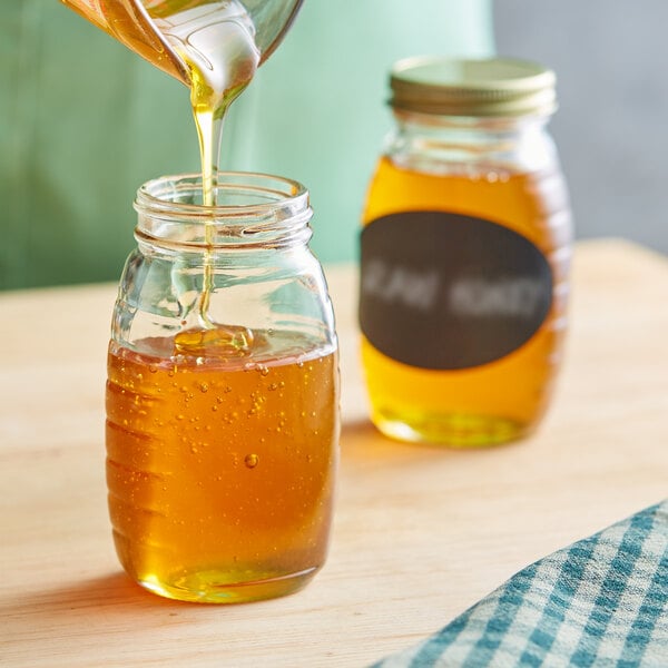 A person pouring honey into a classic Queenline glass jar.