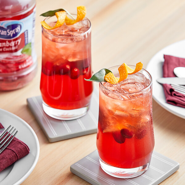 A table with two glasses of Ocean Spray Cranberry Juice Cocktail with ice and cherries.