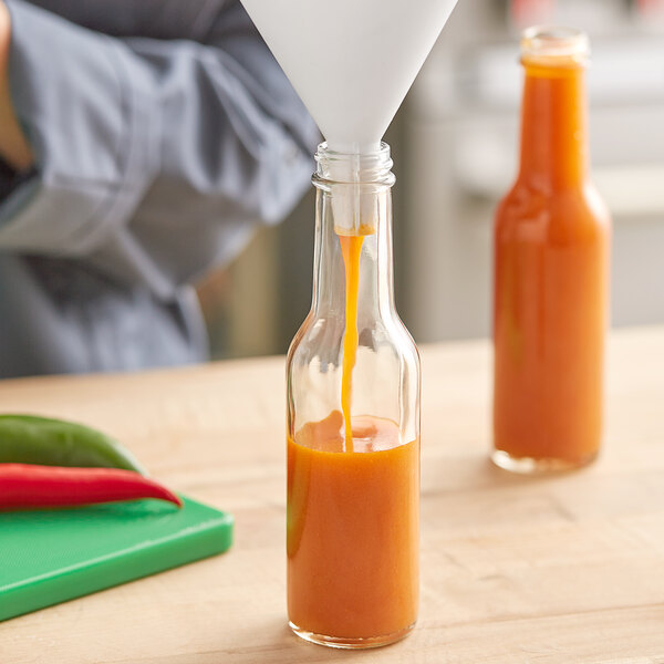 A close-up of orange liquid being poured into a 5 oz. glass Woozy bottle.