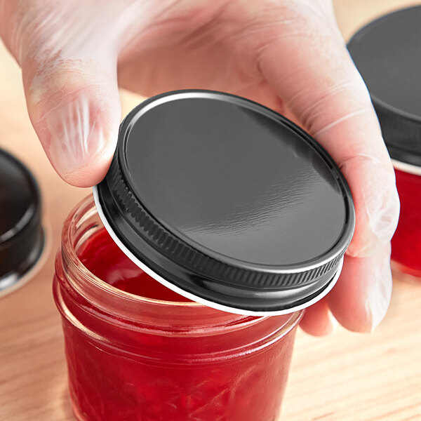 A person's hand using a black metal lid to close a jar of red liquid.