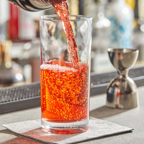 A bartender pouring red liquid into an Acopa beverage glass.