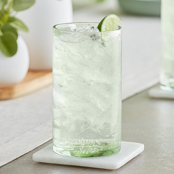A close-up of a green Acopa Pangea beverage glass filled with water, ice, and a lime wedge.