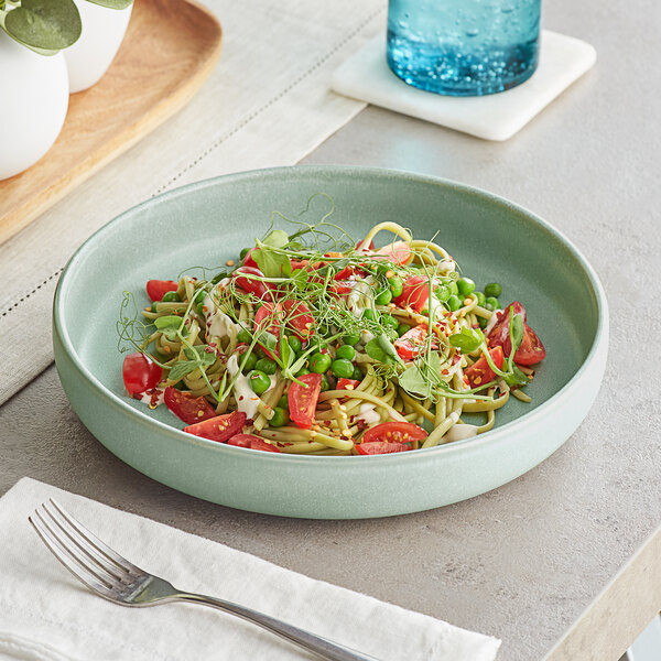 A bowl of pasta with tomatoes, peas, and sprouts in an Acopa Harbor Blue Matte porcelain pasta bowl.