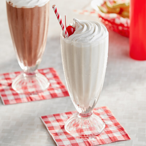 A close-up of two Acopa soda glasses filled with milkshakes topped with whipped cream and cherries.