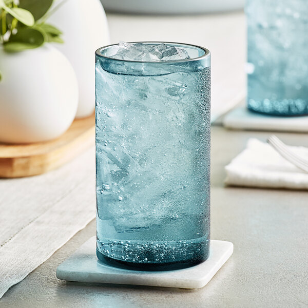 A blue Acopa Pangea beverage glass filled with ice water sitting on a table coaster.