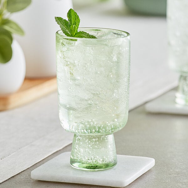 An Acopa Pangea green goblet with ice, mint, and lime on a table.