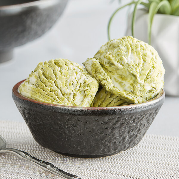 A close-up of a black Acopa Heika stoneware bowl with green ice cream and a spoon.