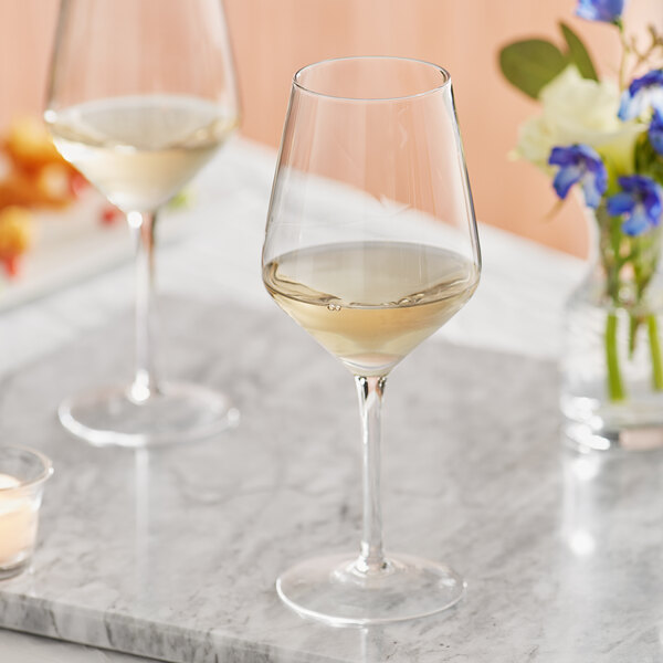 Two Acopa Silhouette wine glasses on a marble table with a glass of white wine.