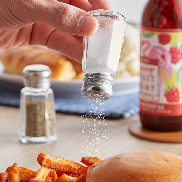A hand holding a Choice mushroom top salt shaker over a plate of food with fries.