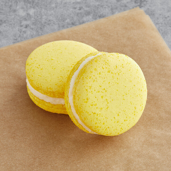Two yellow Macaron Centrale vegan butterbeer macarons on a brown surface.