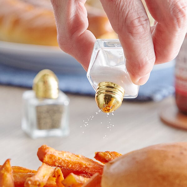 A hand holding a Choice mini salt shaker pouring salt onto a sandwich.