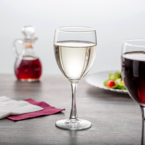 A close-up of a customizable Arcoroc tall wine glass filled with white wine on a table.