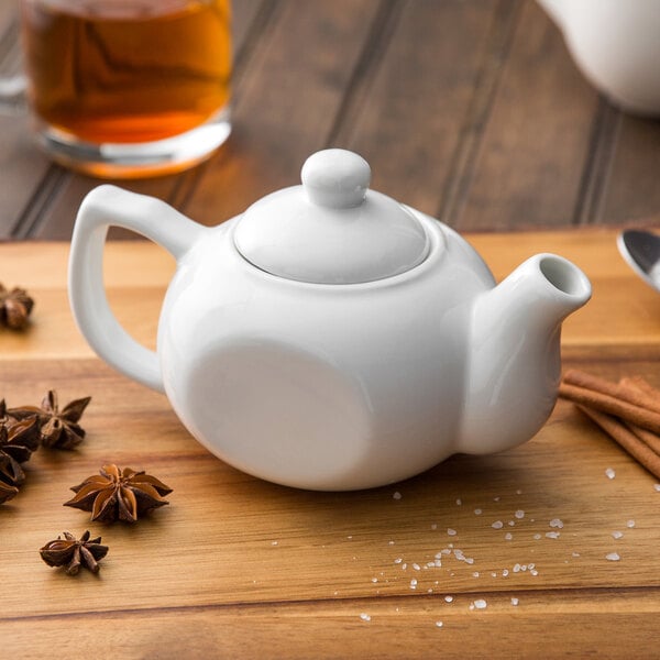 A white Acopa porcelain teapot on a wooden table with spices.