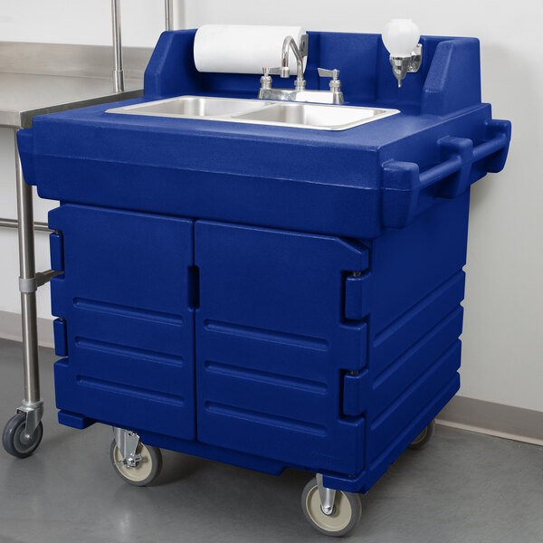 A navy blue plastic Cambro CamKiosk portable sink with wheels.