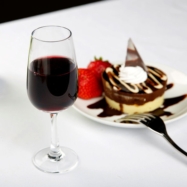A Chef & Sommelier port wine glass filled with red wine next to a plate of dessert.