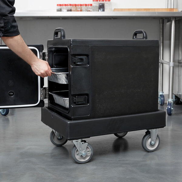 A person using a black Cambro Camdolly to move a metal container.