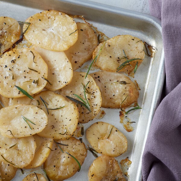 Sliced white potatoes with rosemary on a pan.