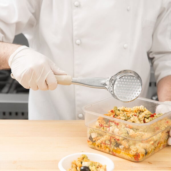 A chef using a Vollrath ivory perforated round Spoodle to serve pasta.