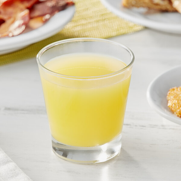 A glass of Dole pineapple juice on a table with breakfast food.