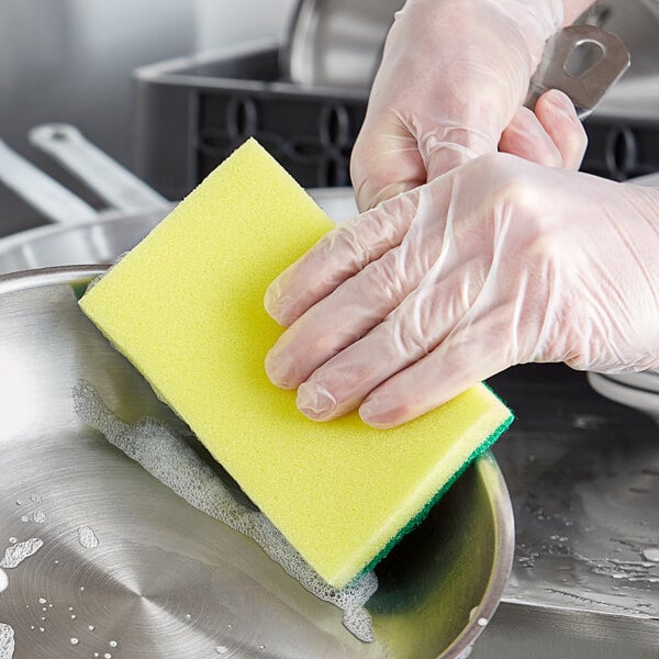 A person in gloves scrubbing a sink with a yellow sponge.