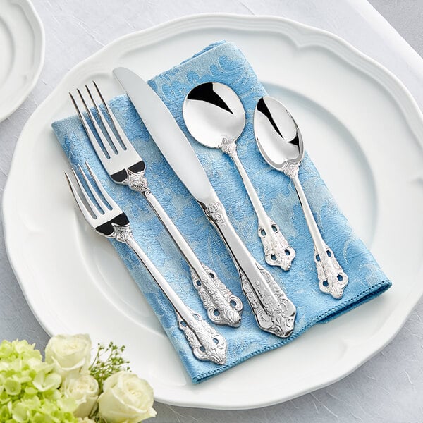 A white plate with Acopa Ophelia stainless steel flatware on a blue surface.