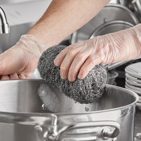 A person using a Choice stainless steel scrubber to clean a pot.