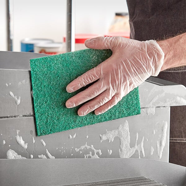 A person in gloves cleaning a metal surface with a green Lavex scouring pad.